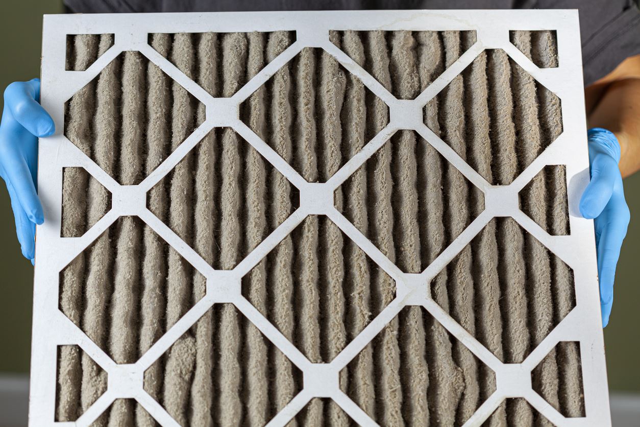 A pair of hands in blue plastic gloves holding a dirty air filter